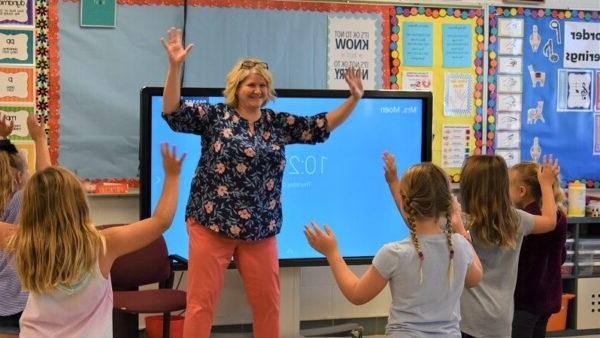 music teacher and students holding their arms up while moving to the beat of a song